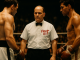 En boxningsdomare från 1950-talet i vit skjorta och svart fluga står mellan två boxare i en upplyst ring med suddig publik i bakgrunden. På bröstet syns loggan Fight Nytt.